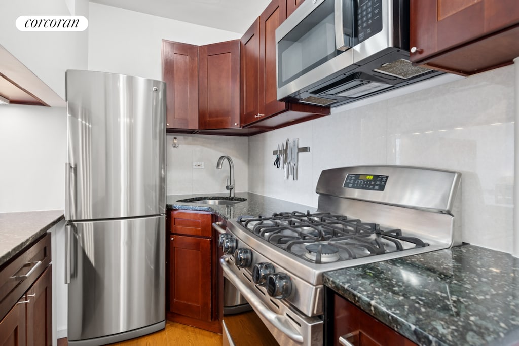 10 W 15th St Unit 1822, New York City, NY 10011 - kitchen with appliances with stainless steel finishes, a sink, tasteful backsplash, dark stone counters, and light wood-style floors