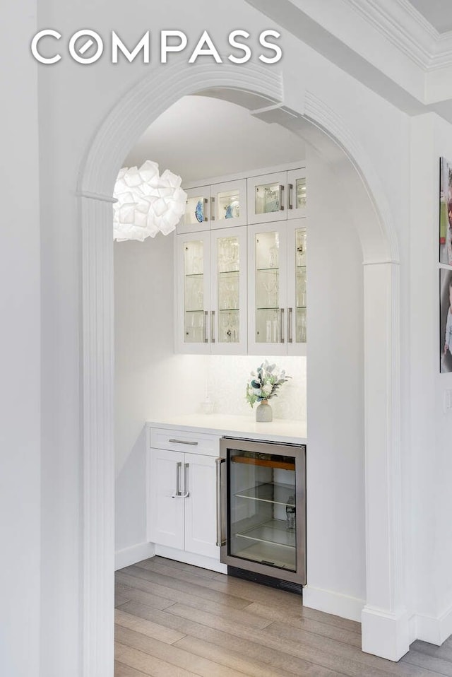 201 E 80th St Unit 16E, New York City, NY 10075 - bar with beverage cooler, light wood-type flooring, arched walkways, crown molding, and baseboards