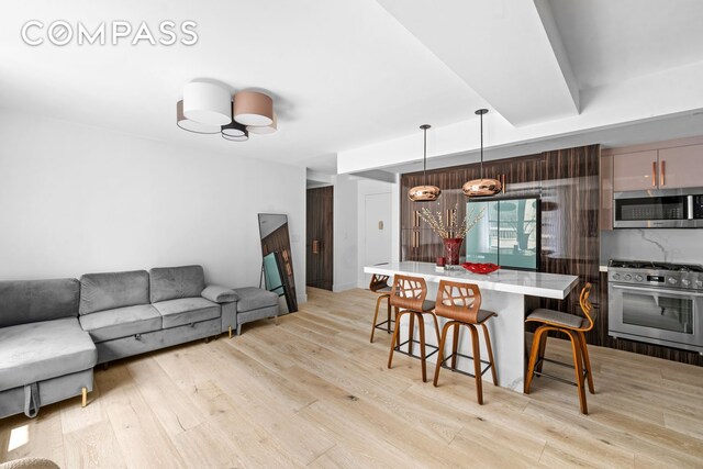 201 W 74th St Unit 8G, New York City, NY 10023 - kitchen featuring stainless steel appliances, light wood-style flooring, a breakfast bar area, light countertops, and pendant lighting