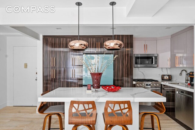 201 W 74th St Unit 8G, New York City, NY 10023 - kitchen featuring stainless steel appliances, a sink, light wood-style flooring, and a kitchen breakfast bar