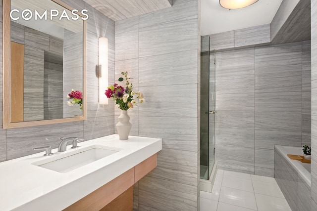 142 E 16th St Unit 22B, New York City, NY 10003 - bathroom featuring tile walls, tile patterned floors, vanity, a garden tub, and a shower with door