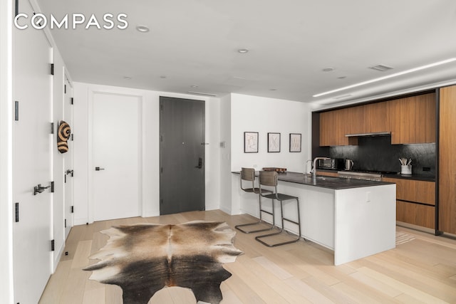 856 Washington Ave Unit 5A, New York City, NY 11238 - kitchen with brown cabinetry, modern cabinets, dark countertops, a kitchen breakfast bar, and decorative backsplash