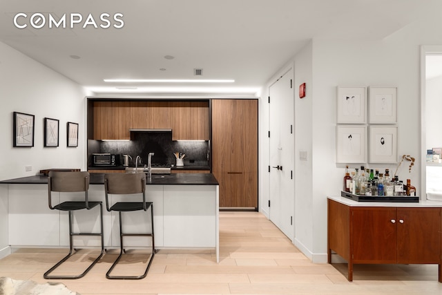 856 Washington Ave Unit 5A, New York City, NY 11238 - kitchen featuring brown cabinets, tasteful backsplash, a kitchen breakfast bar, and dark countertops
