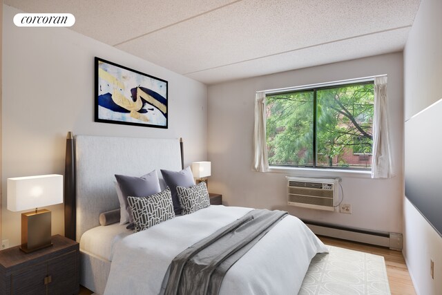 333 E 119th St Unit 1A, New York City, NY 10035 - bedroom with a wall unit AC, wood finished floors, baseboard heating, and a textured ceiling
