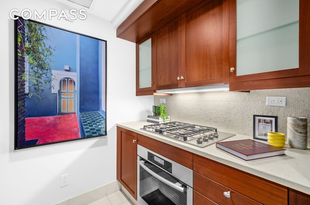 140 E 63rd St Unit 9B, New York City, NY 10065 - kitchen featuring appliances with stainless steel finishes, decorative backsplash, light countertops, light tile patterned flooring, and glass insert cabinets