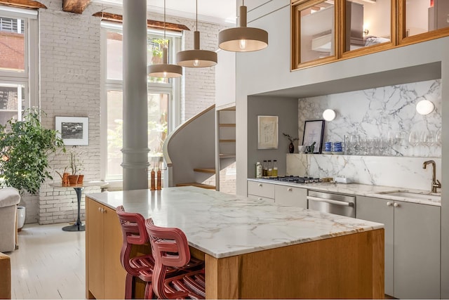 132 Greene St Unit 3R, New York City, NY 10012 - kitchen with a sink, brick wall, light stone counters, stainless steel appliances, and a center island