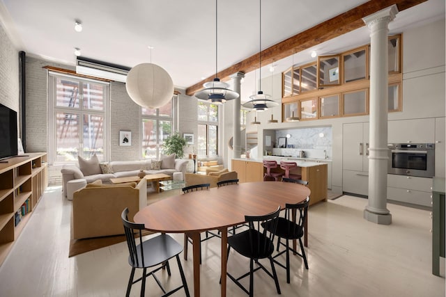132 Greene St Unit 3R, New York City, NY 10012 - dining area featuring ornate columns, light wood-style flooring, beamed ceiling, and a high ceiling