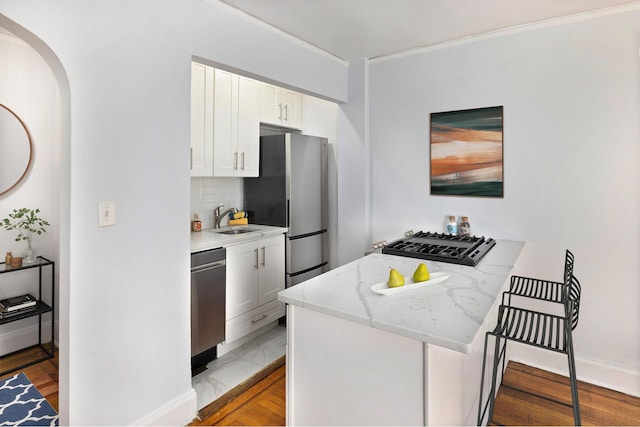 240 E 24th St Unit 2H, New York City, NY 10010 - kitchen with appliances with stainless steel finishes, a peninsula, arched walkways, white cabinetry, and decorative backsplash