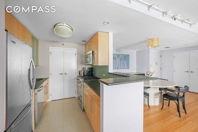 40 W 116th St Unit B302, New York City, NY 10026 - kitchen featuring stainless steel appliances, a peninsula, dark countertops, a kitchen breakfast bar, and decorative backsplash