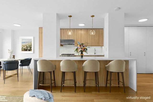 7 E 14th St Unit 905, New York City, NY 10003 - kitchen featuring under cabinet range hood, modern cabinets, light countertops, decorative backsplash, and a breakfast bar area