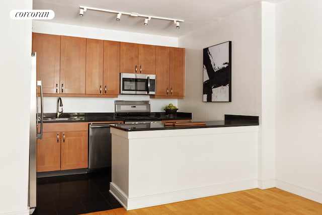 99 Jane St Unit 2J, New York City, NY 10014 - kitchen with appliances with stainless steel finishes, a sink, dark countertops, a peninsula, and brown cabinetry