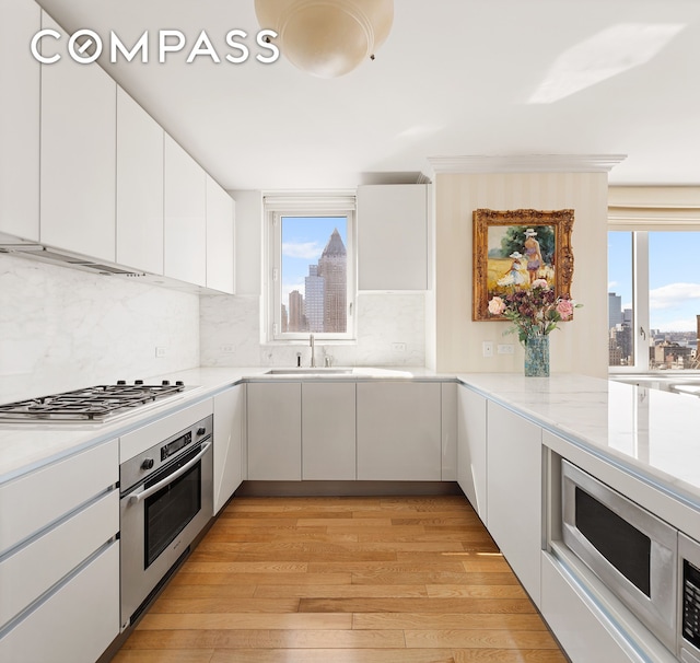 322 W 57th St Unit 33U, New York City, NY 10019 - kitchen featuring appliances with stainless steel finishes, a skyline view, light wood finished floors, decorative backsplash, and white cabinetry