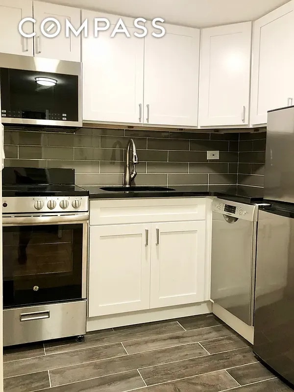 80 Park Ave Unit 12F, New York City, NY 10016 - kitchen with appliances with stainless steel finishes, wood tiled floors, white cabinets, and dark countertops