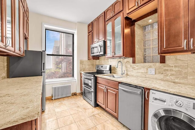 350 W 48th St Unit 1W, New York City, NY 10036 - kitchen featuring washer / clothes dryer, stainless steel appliances, radiator, a sink, and light stone countertops