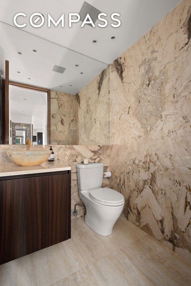 303 E 57th St Unit 33Ef, New York City, NY 10022 - bathroom featuring vanity, toilet, stone wall, and marble finish floors