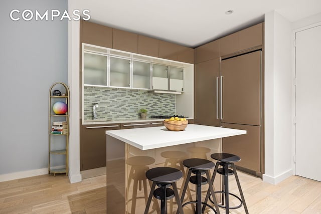 75 Wall St Unit 25K, New York City, NY 10005 - kitchen with a kitchen bar, light wood finished floors, tasteful backsplash, and glass insert cabinets
