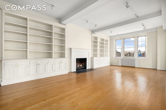 45 Christopher St Unit 12/14F, New York City, NY 10014 - unfurnished living room featuring track lighting, radiator heating unit, a brick fireplace, and light wood-type flooring