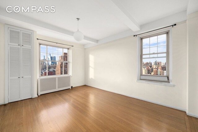 45 Christopher St Unit 12/14F, New York City, NY 10014 - unfurnished bedroom with radiator, hardwood / wood-style floors, beamed ceiling, a closet, and a city view