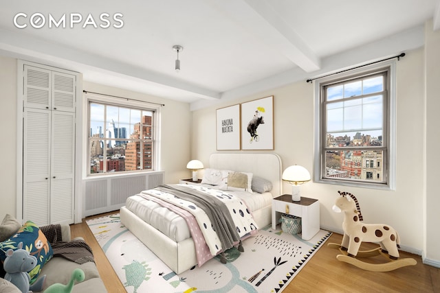 45 Christopher St Unit 12/14F, New York City, NY 10014 - bedroom featuring radiator, beam ceiling, wood finished floors, a view of city, and a closet