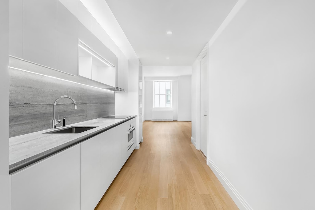 1 Wall St Unit 932, New York City, NY 10005 - kitchen with white cabinetry, modern cabinets, light wood-style floors, backsplash, and light countertops