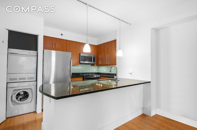 242 E 25th St Unit 5B, New York City, NY 10010 - kitchen with stainless steel appliances, stacked washer and clothes dryer, a sink, a peninsula, and light wood finished floors