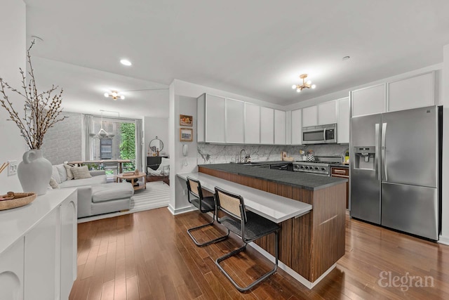 130 W 19th St Unit 4F, New York City, NY 10011 - kitchen featuring stainless steel appliances, a peninsula, a kitchen breakfast bar, dark countertops, and dark wood-style floors