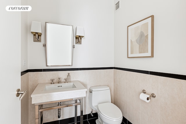 151 E 58th St Unit 42C, New York City, NY 10022 - half bathroom featuring toilet, tile walls, a wainscoted wall, and a sink