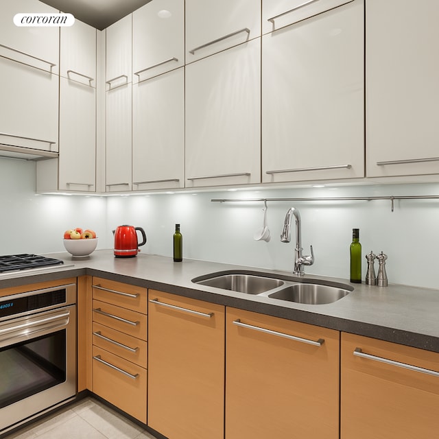 151 E 58th St Unit 42C, New York City, NY 10022 - kitchen with stainless steel appliances, a sink, white cabinetry, dark countertops, and light tile patterned flooring