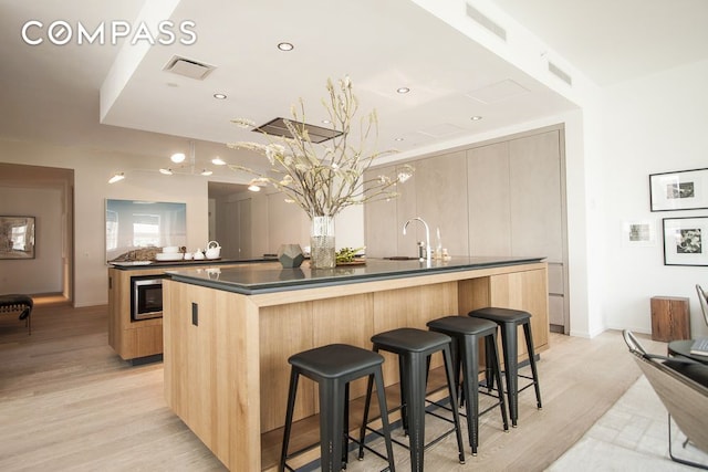 1 John St Unit 3B, New York City, NY 11201 - kitchen with a large island with sink, dark countertops, modern cabinets, light wood finished floors, and a kitchen bar