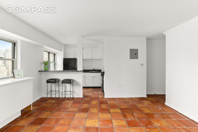 609 Columbus Ave Unit 14E, New York City, NY 10024 - kitchen with fridge, electric panel, white cabinetry, dark countertops, and a breakfast bar