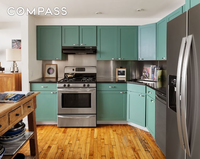 138 Broadway Unit 1D, New York City, NY 11211 - kitchen with stainless steel appliances, under cabinet range hood, a sink, dark countertops, and light wood-style flooring