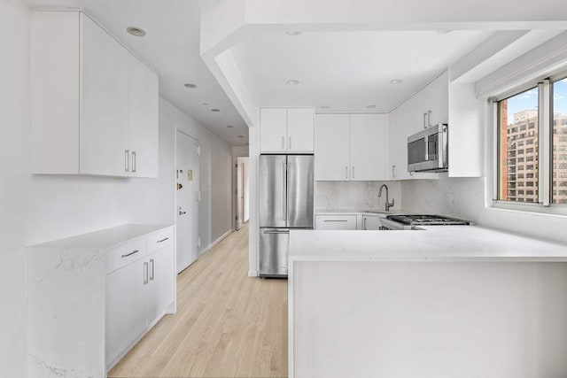 137 E 13th St Fl 9Th, New York City, NY 10003 - kitchen featuring stainless steel appliances, light wood-style floors, a peninsula, white cabinets, and a sink