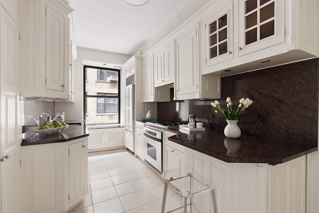 50 Riverside Dr Unit 10B, New York City, NY 10024 - kitchen with appliances with stainless steel finishes, light tile patterned floors, backsplash, dark countertops, and glass insert cabinets