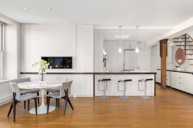 10 Bleecker St Unit 7A, New York City, NY 10012 - kitchen with wood finished floors, white cabinetry, a glass covered fireplace, a breakfast bar, and hanging light fixtures