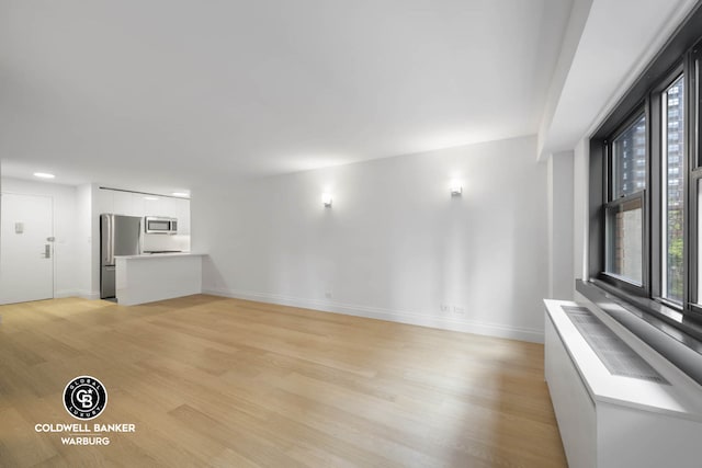 235 E 87th St Unit 7E, New York City, NY 10128 - unfurnished living room featuring plenty of natural light, light wood-style flooring, and baseboards