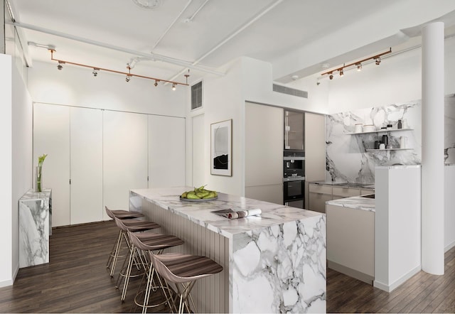 152 Wooster St Unit 2A, New York City, NY 10012 - kitchen featuring rail lighting, dark wood finished floors, light stone countertops, a breakfast bar, and a kitchen island