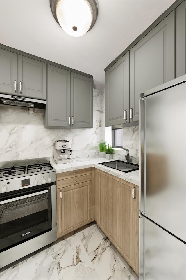 2 W 90th St Unit 2C, New York City, NY 10024 - kitchen with appliances with stainless steel finishes, gray cabinets, under cabinet range hood, a sink, and light marble finish flooring