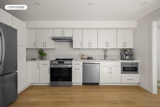 291 6th Ave Unit 1, New York City, NY 11215 - kitchen featuring appliances with stainless steel finishes, under cabinet range hood, light countertops, light wood-type flooring, and white cabinetry