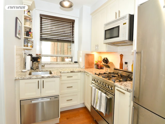 333 E 43rd St Unit 511, New York City, NY 10017 - kitchen featuring stainless steel appliances, backsplash, a sink, light wood-style flooring, and light stone countertops