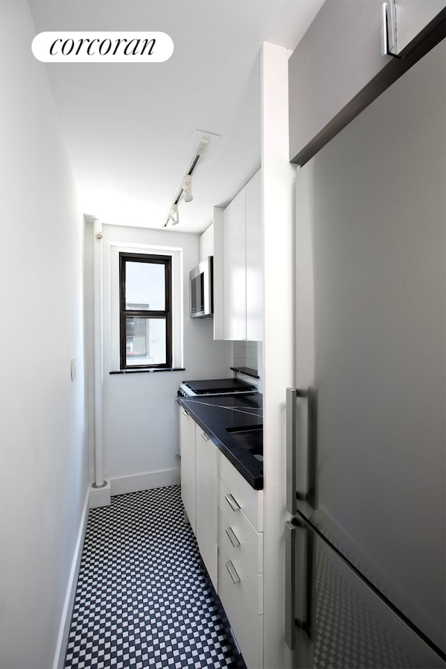 240 E 24th St Unit 4B, New York City, NY 10010 - kitchen featuring appliances with stainless steel finishes, dark countertops, white cabinetry, baseboards, and dark floors