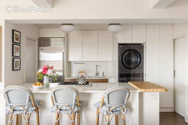 200 E 16th St Unit 14C, New York City, NY 10003 - kitchen featuring stacked washer and clothes dryer, a sink, appliances with stainless steel finishes, a breakfast bar, and backsplash
