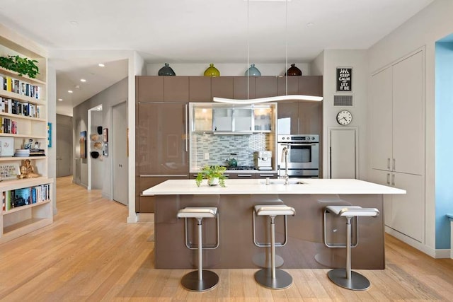 75 Wall St Unit 21N/O, New York City, NY 10005 - kitchen featuring light wood finished floors, a kitchen breakfast bar, backsplash, a kitchen island with sink, and recessed lighting