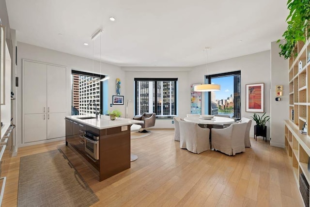 75 Wall St Unit 21N/O, New York City, NY 10005 - kitchen featuring a sink, stainless steel oven, light wood-style floors, decorative light fixtures, and a kitchen island with sink
