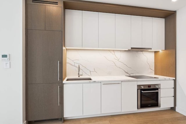 45-30 Pearson St Unit 6F, New York City, NY 11101 - kitchen with stainless steel oven, black electric cooktop, a sink, decorative backsplash, and white cabinetry