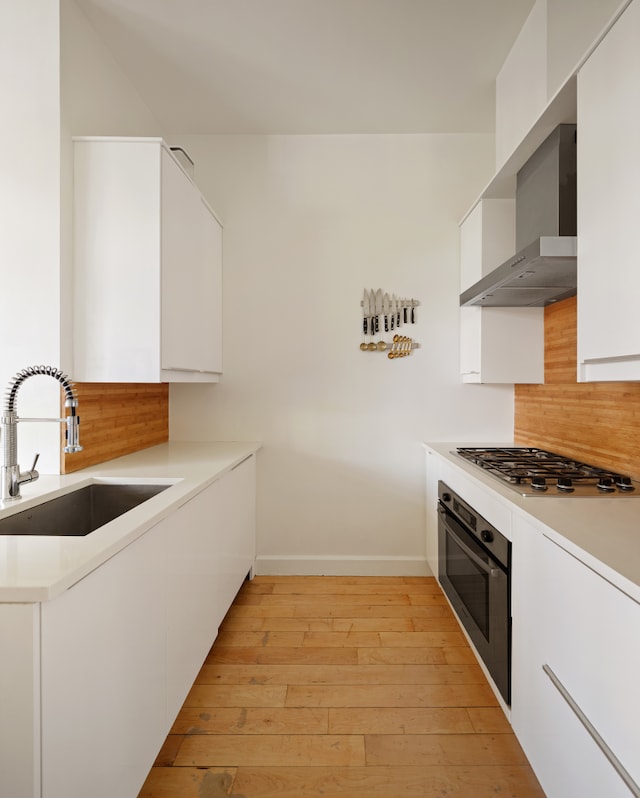 136 Powers St Unit 1G, New York City, NY 11211 - kitchen featuring wall oven, wall chimney range hood, a sink, white cabinets, and baseboards