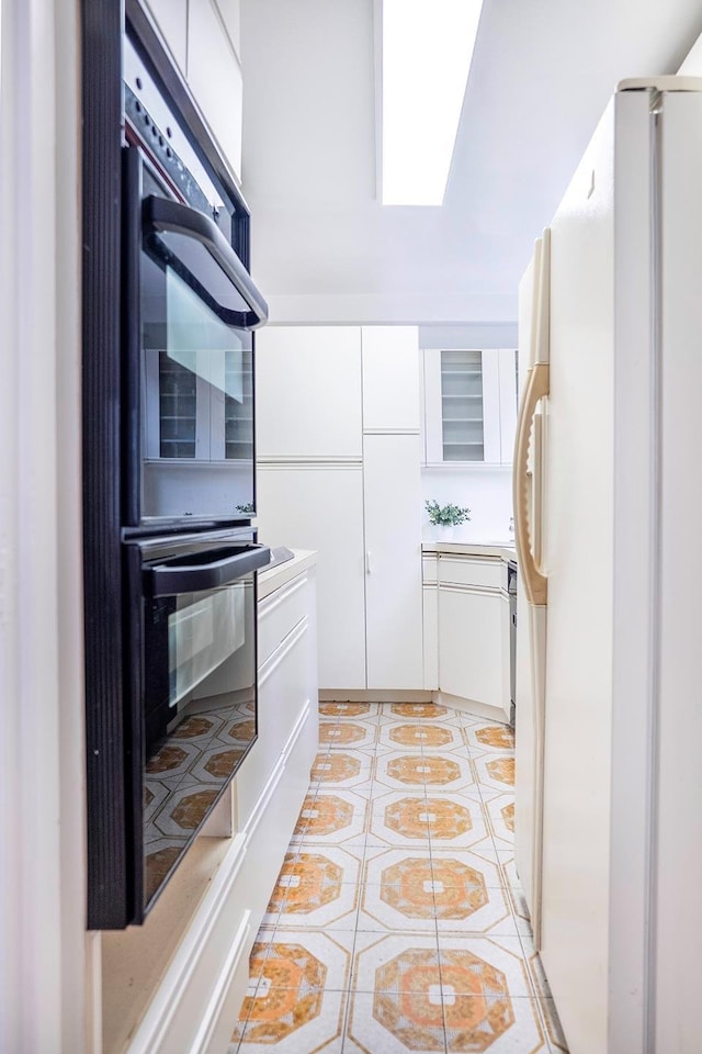 77 W 55th St Unit 4B, New York City, NY 10019 - kitchen with freestanding refrigerator, white cabinets, light tile patterned floors, and light countertops