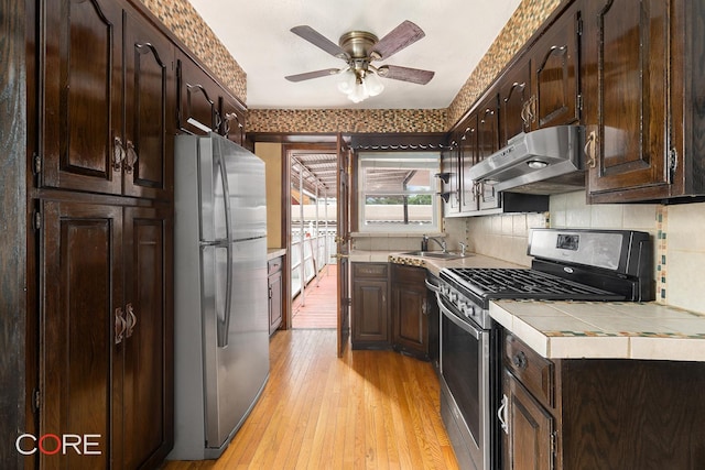 3707 Quentin Rd, New York City, NY 11234 - kitchen with stainless steel appliances, under cabinet range hood, tile counters, dark brown cabinets, and light wood-type flooring