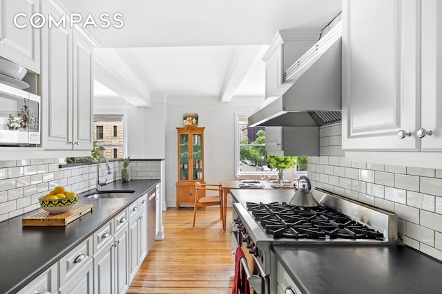 49 E 96th St Unit 4D, New York City, NY 10128 - kitchen featuring appliances with stainless steel finishes, dark countertops, light wood finished floors, white cabinetry, and beamed ceiling
