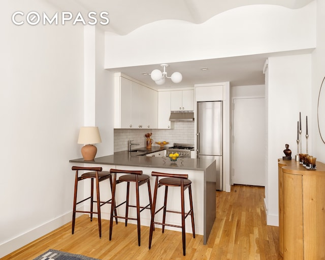 9 Barrow St Unit 3C, New York City, NY 10014 - kitchen with stainless steel fridge, under cabinet range hood, a peninsula, white cabinets, and light wood-style floors