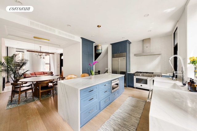 181 Waverly Ave, New York City, NY 11205 - kitchen with wall chimney exhaust hood, built in appliances, blue cabinets, a sink, and light wood-type flooring